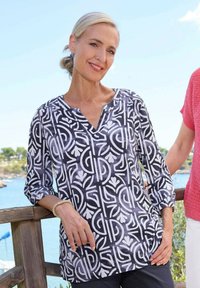 Schwarz-weiß bedruckte Bluse mit V-Ausschnitt, 3/4-Rollenärmeln und lockerer Passform. Verziert mit einem geometrischen und floralen Muster.