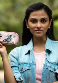 Roze leren portemonnee met bloem- en vlinderborduursel, ronde vorm met een ritsluiting, vastgehouden door een persoon in een spijkerjack.