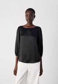 Zwarte satijnen blouse met lange mouwen en een ronde halslijn, met puffmouwen en een gladde textuur. Gemaakt om te dragen met losse witte broeken.