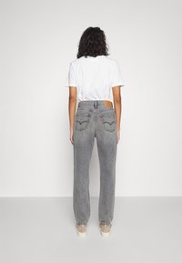 Jeans de talle alto grises con una textura ligera, que cuentan con bolsillos traseros y una etiqueta de cuero en la cinturilla. Combinados con una camiseta blanca.