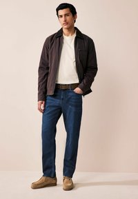 Jachetă crem cu fermoar, cu guler din catifea, cămașă albă, blugi drepti de culoare albastră și pantofi din suede tan. Design simplist, îmbrăcăminte casual.