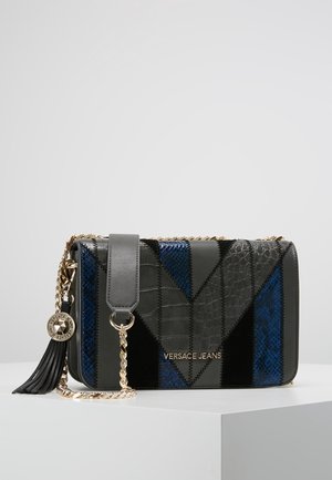 Sort og blå patchwork læder Versace Jeans skuldertaske med guldkæde, kvast og logohæng på hvidt underlag.