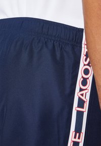 Pantalones cortos deportivos en color marino con tejido texturizado, cintura elástica y franjas laterales blancas contrastantes con letras rojas.