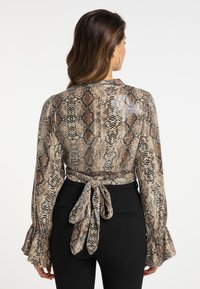 Langærmet bluse i slangemønster med beige, brune og sorte nuancer. Har en knyttet talje og flared ærmer; tekstureret stof.
