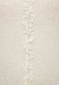Cremefarbener Strickstoff mit einer zentralen strukturierten Naht, die weiche, erhabene Fäden aufweist und ein kontrastierendes visuelles Detail bietet.