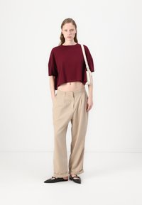 Burgundská zkrácená halenka, béžové široké kalhoty s plisováním a černé špičaté baleríny. Minimalistická ramenní taška v světlé barvě. Čistý, moderní vzhled.