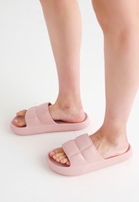 Pink rubber slides with a thick, textured sole and a wide strap featuring a quilted pattern. Open-toed design for easy wear.