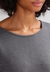 Maglia grigia con una texture a coste, caratterizzata da una scollatura ampia e un tessuto morbido, che mette in evidenza la luce sottile e il colore uniforme.