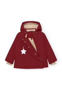 Chaqueta impermeable roja con forro de felpa beige, capucha y botones a presión prominentes; incluye una etiqueta con forma de estrella en el tirador de la cremallera.