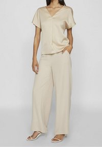 Beige satin-topp med V-ringning och korta ärmar, kombinerad med vida beige byxor. Outfiten har en mjuk textur och avslappnad passform.