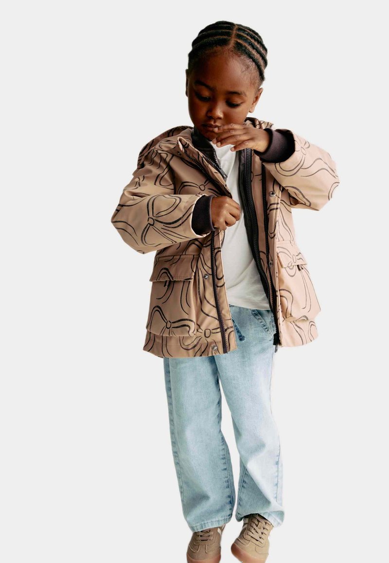 Brun mønstret jakke med hætte, lynlås og sidelommer, parret med lyseblå jeans og beige sneakers.