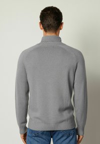 Grå stickad tröja med hög krage, ribbade ärmslut och nederkant. Slät textur med raglanärmar och inga synliga mönster.