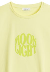 Jasnożółta koszulka z okrągłym dekoltem, z wyraźnym zielonym napisem "MOON LIGHT" w zabawnym kroju czcionki, umieszczonym na środku z przodu.