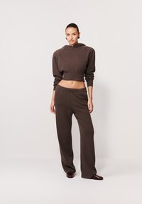 Brązowy krótki hoodie z kapturem i szerokimi rękawami, zestawiony z dopasowanymi luźnymi spodniami. Gładka dzianinowa tekstura; minimalistyczny design.