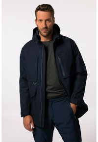 Tummansininen parka-takki, jossa on huppu, useita taskuja, etuvetoketju ja pintakuvio. Päällä tummanharmaa paita.