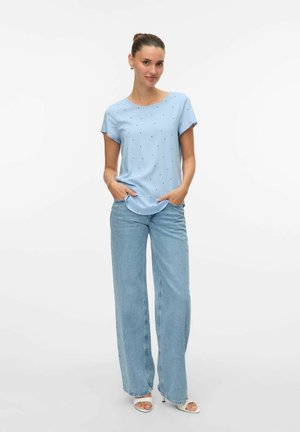 Light blue short-sleeve top with scattered black dots, paired with high-waisted light denim wide-leg pants. Smooth fabric with a relaxed fit.