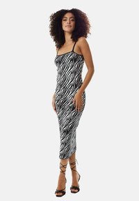 Black and white zebra striped midi dress with thin straps, fitted design, and a smooth texture, paired with strappy black heels.