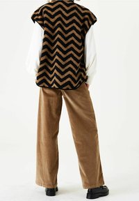 Fleecväst med svart och brunt zigzag-mönster, tillsammans med tanfärgade kordflortbyxor. Svarta chunky stövlar fulländar outfiten.