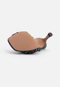 Musta nahkakengät, joissa on joustava, kerätty päällinen ja sileä, vaalea kumipohja, jossa on teksturoitu pito kantapäässä.