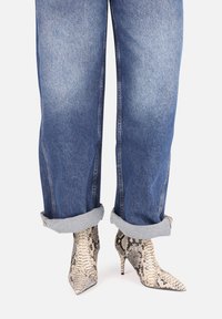 Špičaté hadí vzorované lodičky s texturovaným povrchem, v kombinaci s ohrnutými, světle modrými džíny s uvolněným střihem.