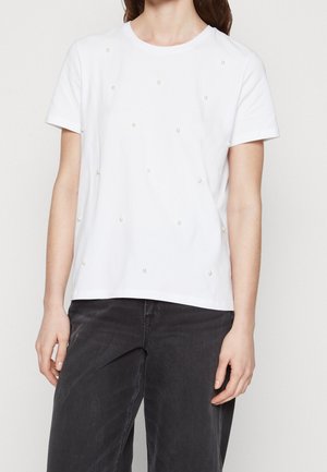 Camiseta de algodón blanca con mangas cortas, con bonitos acentos decorativos de perlas espaciados de manera uniforme en la parte delantera. Cuello redondo sencillo.