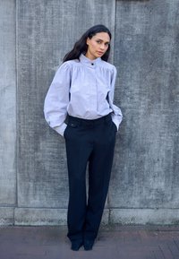 Jasnoszara bluzka z długim rękawem, bufkami na ramionach i wysokim kołnierzem, zestawiona z czarnymi spodniami z wysokim stanem. Gładkie tekstury i dopasowany krój.