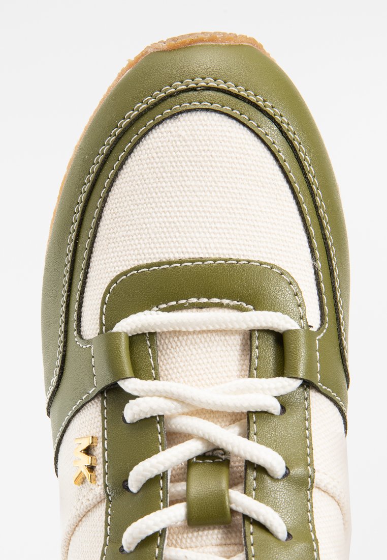 Primo piano della punta di una sneaker con rete bianca, rifiniture in pelle verde oliva, lacci bianchi e logo dorato MK sul lato.