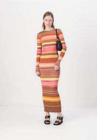 Abito a maniche lunghe a coste con righe orizzontali nei colori rosa, arancione, marrone e giallo. Chi lo indossa tiene in mano una piccola borsa nera. Sandali neri con tacco.