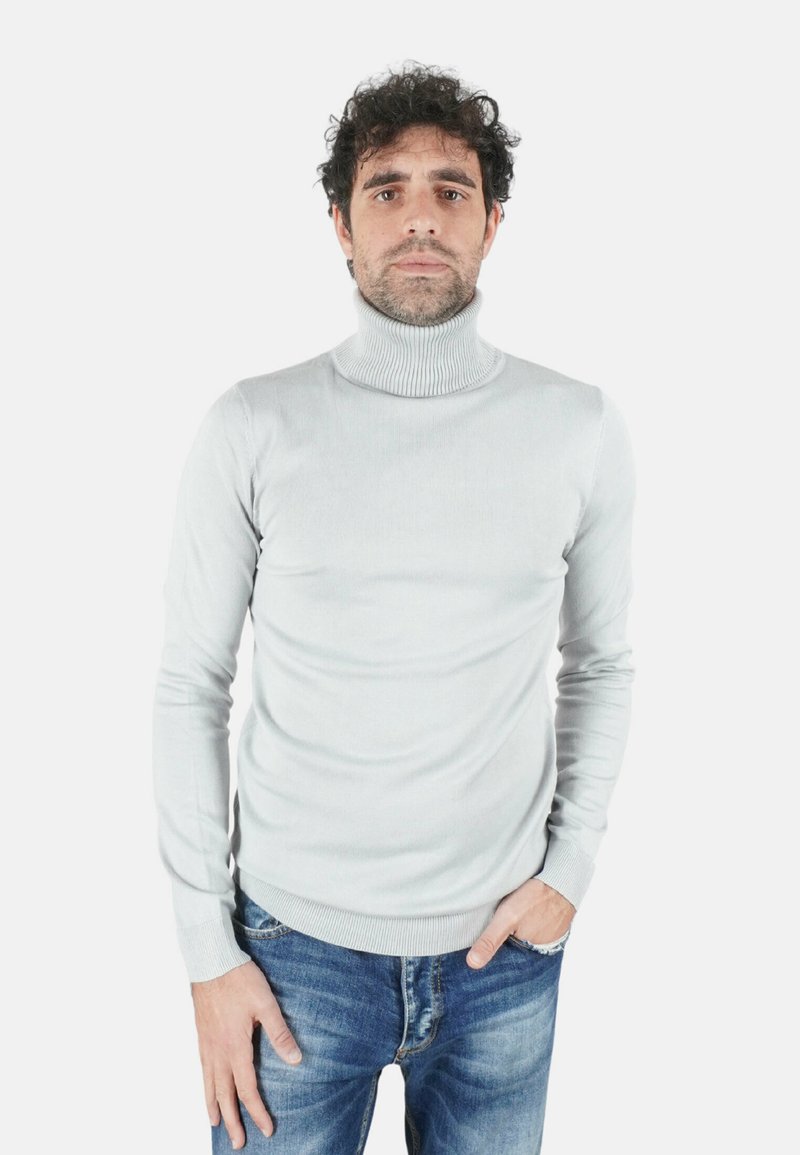 Maglione dolcevita grigio chiaro con texture a coste e design aderente, abbinato a jeans blu. Il maglione presenta maniche lunghe e collo alto.