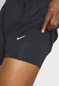 Zwarte sportieve shorts van lichtgewicht stof met een elastische tailleband. Heeft een klein zilveren Nike-logo aan de linkerkant en zichtbare stiksels.