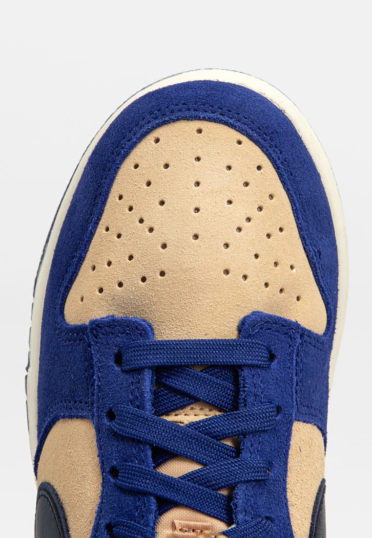 Zapatilla azul y beige con parte superior de ante, caja de dedos perforada, cordones planos y suela de goma blanca. Los acentos texturizados mejoran el diseño.