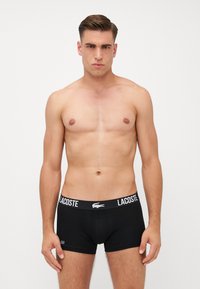 Boxer shorts Lacoste negros con una cinturilla de logo blanco. La tela parece suave y ajustada, sin patrones ni costuras visibles.