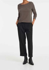 Svartvit prickig långärmad topp kombinerad med höga svarta byxor med uppvikta muddar och svarta kängor.