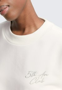 Witte sweatshirt met geribbelde halslijn en geborduurd logo "5th Ave Clark" in zilver. Zachte stof met een gladde textuur.
