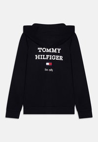 Sudadera negra con capucha de algodón que presenta "TOMMY HILFIGER" en texto blanco en la parte trasera, junto con un pequeño logo y "Est. 1985" debajo.