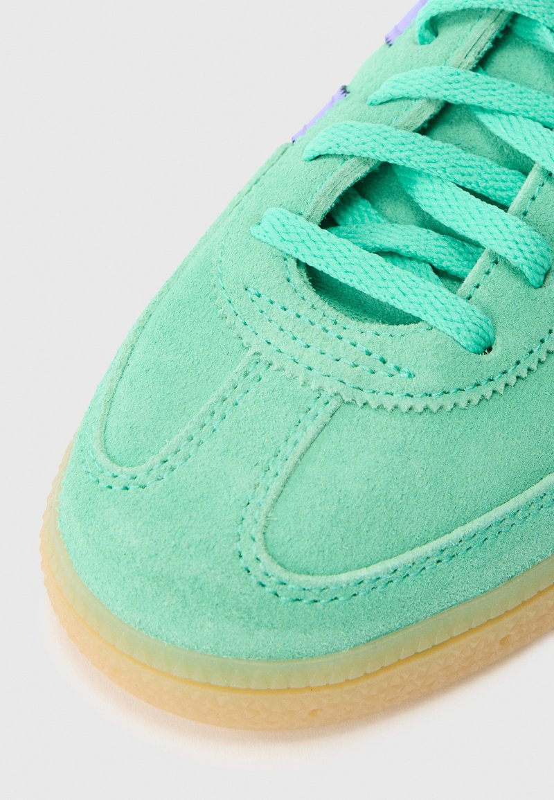 Light green suede sneaker with matching laces, rounded toe, and gum rubber sole. Features stitched detailing and a smooth texture.