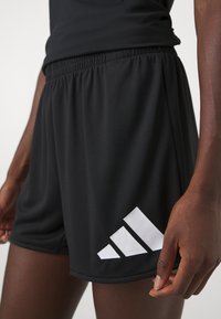 Mustad sportlikud lühikesed püksid, millel on tekstureeritud kangas, elastne vöökoht ja suur valge adidas logo vasakul küljel.