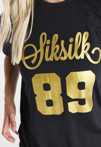 Černý dres se zlatým logem "Siksilk" a číslem "89". Disponuje strukturovaným, prodyšným materiálem a designem s kruhovým výstřihem.