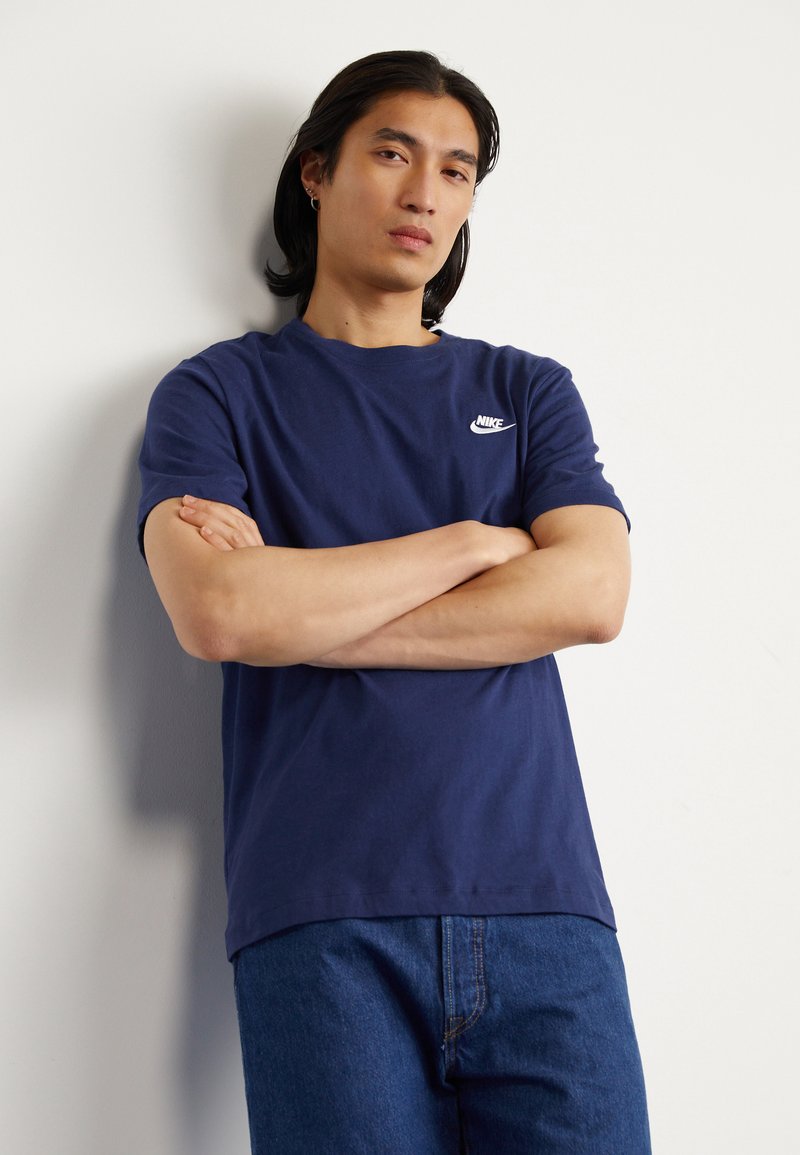 Tumši zilas krāsas kokvilnas t-krekls ar īsām piedurknēm, uz kura krūtīm ir baltais Nike logo. Piegriezums ir parasts, ar gludu tekstūru.