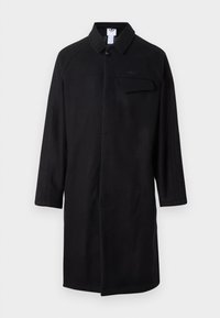 Cappotto nero con colletto, maniche lunghe, chiusura a un bottone e tasca sul petto. Presenta pannelli laterali testurizzati.