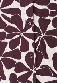 Chemise boutonnée avec de grandes formes florales abstraites violet foncé sur fond blanc, avec des coutures piquées le long de la patte de boutonnage.
