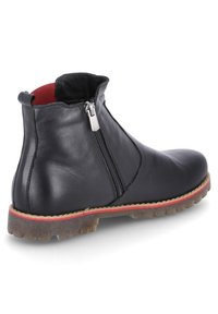 Botín de cuero negro con acabado texturizado, cremallera lateral, forro interior rojo y detalle de suela roja en contraste.