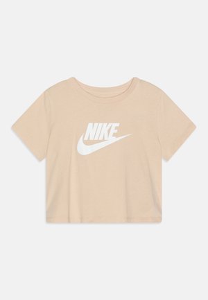 Beige crop top met korte mouwen, met een wit Nike-logo en swoosh gecentreerd aan de voorkant, weergegeven op een effen lichte achtergrond.