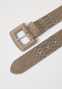 Harmaa nahkavyö, jossa on textured, skaala-tyylinen kuvio. Siinä on neliön muotoinen solki, jossa on hopeanvärinen metallitappi ja useita säätöreikiä.