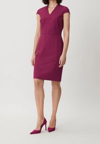 Figurbetontes, kurzärmliges Kleid in tiefem Magenta, V-Ausschnitt-Design, glattes synthetisches Gewebe, knielang, kombiniert mit passenden High Heels.