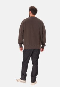 Felpa oversize marrone scuro con scollo rotondo, polsini e orlo a costine, abbinata a jeans in denim scuro e sneaker color avorio.
