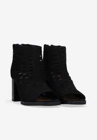 Botas negras hasta el tobillo fabricadas con un tejido suave y con detalles recortados. Diseño de punta abierta, tacón cuadrado y superficie texturizada.