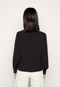 Chemise noire à manches longues avec des détails froncés aux épaules et aux poignets. La vue arrière montre une texture lisse et un ourlet droit.