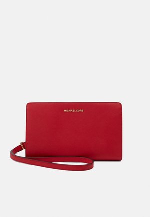 Rød Michael Kors håndledslommebog med gult logo og håndledsrem på en ensfarvet lys baggrund.