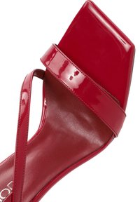 Sandale à talons hauts en cuir verni rouge avec un orteil carré, une fine sangle autour de la cheville et une texture lisse et brillante sur le dessus.
